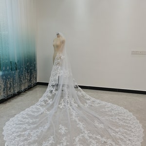 Puede incluir: Un velo de novia blanco con delicado bordado de encaje y un borde festoneado. El velo se muestra en un maniqu&iacute; en una habitaci&oacute;n blanca.