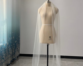 May include: A white tulle wedding veil draped over a dress form. The veil is long and flowing, with a simple design.