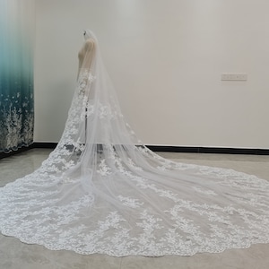 Puede incluir: Un velo de novia largo y blanco con un delicado bordado de encaje floral. El velo est&aacute; hecho de tul suave y tiene un borde festoneado.