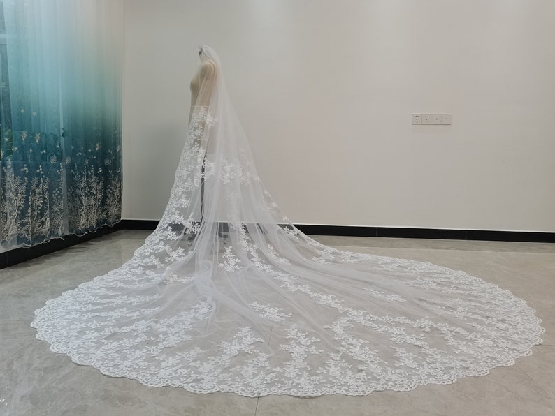 Puede incluir: Un velo de novia largo y blanco con un delicado bordado de encaje floral. El velo est&aacute; hecho de tul suave y tiene un borde festoneado.