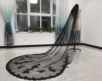 May include: A black tulle wedding veil with a lace trim. The veil is draped over a mannequin and is laying on a white floor.