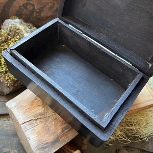 May include: A black wooden box with a hinged lid, open to reveal an empty interior. The box is made of dark wood and has a smooth finish.
