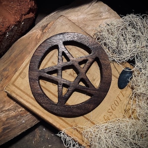 May include: A dark brown wooden pentagram with a five-pointed star design, resting on a vintage book with the text "by SCOTT" visible.