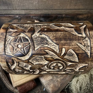 May include: A handcrafted wooden box with intricate carvings. The box features a pentagram and star designs, along with other detailed patterns. The wood has a dark, aged appearance, with visible grain and texture, suggesting a rustic or vintage aesthetic.