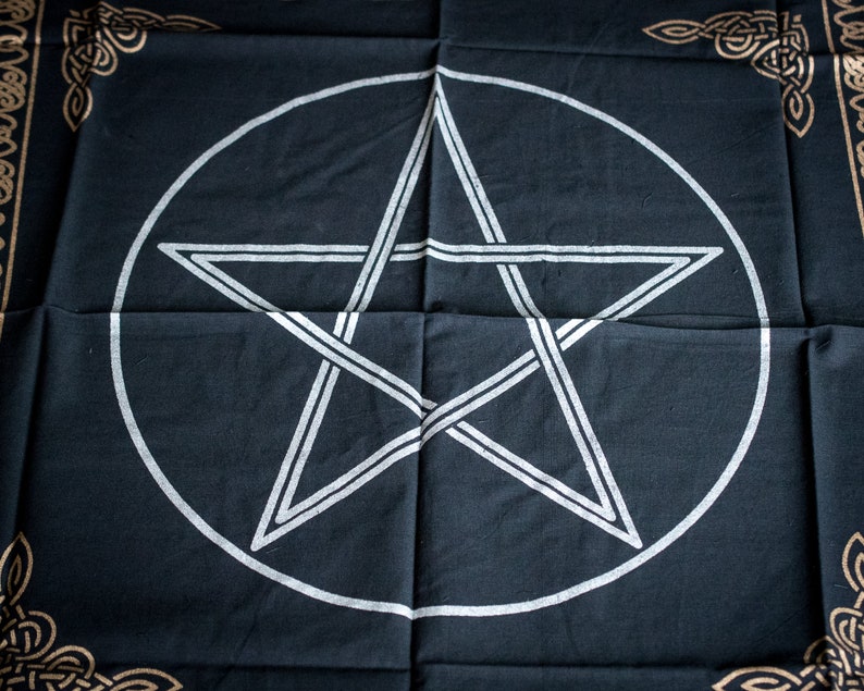 Pu&ograve; includere: Tessuto nero con un pentagramma bianco all'interno di un cerchio. Il tessuto ha un bordo di nodo celtico dorato.