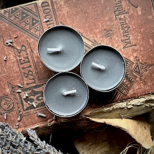 May include: Three gray wax tealights on an old book with the title "Childhood" by "Marchel Tima" on the cover.