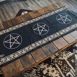 May include: Black altar cloth with a gold border and three white pentagrams. The cloth is laid out on a wooden table.