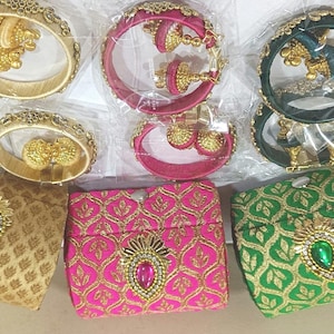 May include: An assortment of ornate jewelry and small fabric pouches. The jewelry includes gold-colored bangles and earrings, along with pink and green bangles and earrings. The pouches are gold, pink, and green, with decorative embellishments.