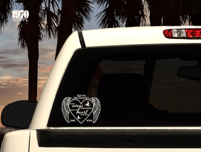 May include: White vinyl decal with a heart shape and angel wings. The text reads "Kevin McDaniel Your wings were ready but my heart was not 1961 2019".