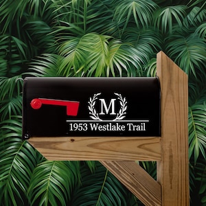 May include: Black mailbox with a white monogram sticker featuring the letter "M" inside a wreath. The text "1953 Westlake Trail" is below the monogram.