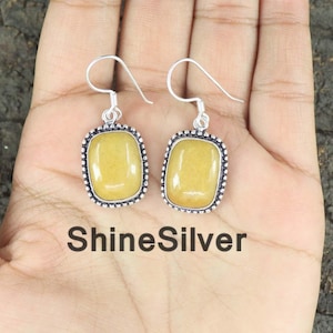 May include: A pair of silver earrings with a square, light yellow stone. The earrings have a beaded border and a hook closure. The text "ShineSilver" is visible below the earrings.