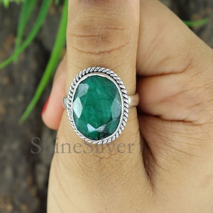May include: A silver ring with a green gemstone set in a twisted rope design band.