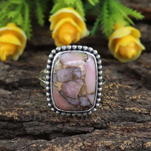 May include: A silver ring with a rectangular pink and gold opal gemstone. The ring is set in a silver bezel with a beaded edge.