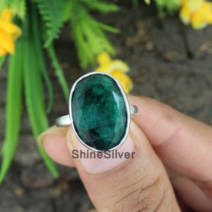 May include: A silver ring featuring a large, oval-shaped, dark green emerald gemstone. The ring is set in a simple, silver band.