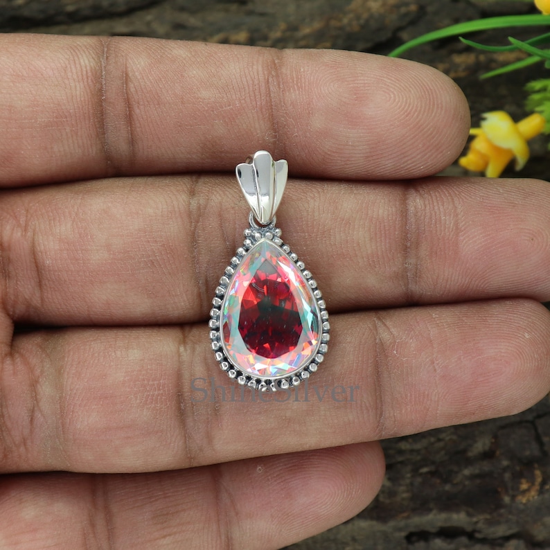 K&ouml;nnte beinhalten: Ein tropfenf&ouml;rmiger Anh&auml;nger mit einem perlmuttartigen roten Edelstein in einer silbernen Fassung. Der Anh&auml;nger ist mit einer Perlenbord&uuml;re verziert.