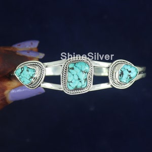 K&ouml;nnte beinhalten: Silberner Armreif mit drei T&uuml;rkis-Steinen. Die Steine sind in Silber gefasst und haben eine strukturierte Oberfl&auml;che. Der Armreif ist offen und verstellbar.