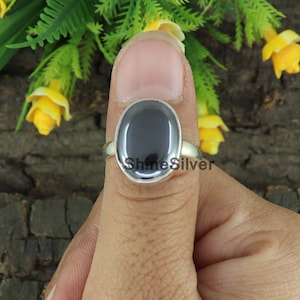 May include: A silver ring with a black oval gemstone. The ring is on a finger.