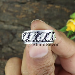 Könnte beinhalten: Ein silberner Ring mit einem drehbaren Band, das mit einem sich wiederholenden Muster aus kleinen, stilisierten Tierfiguren verziert ist. Der Ring wird an einem Finger getragen.