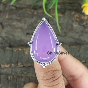 Puede incluir: Un anillo de plata con una piedra preciosa púrpura en forma de lágrima. El anillo está engastado con pequeñas cuentas de plata alrededor de la piedra preciosa.