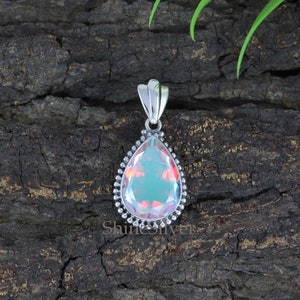 K&ouml;nnte beinhalten: Ein tropfenf&ouml;rmiger, regenbogenfarbener Edelstein-Anh&auml;nger mit einer silbernen Fassung. Der Anh&auml;nger hat einen perlenbesetzten Rand und eine silberne &Ouml;se.