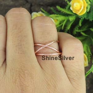 May include: A rose gold ring with a crisscross design. The ring has a textured surface and the text "ShineSilver" is visible on the ring. The ring is on a finger.