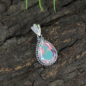 K&ouml;nnte beinhalten: Ein tropfenf&ouml;rmiger Anh&auml;nger mit einem regenbogenfarbenen Edelstein, der in einer silbernen Fassung sitzt. Der Anh&auml;nger hat einen perlenbesetzten Rand und eine silberne &Ouml;se.