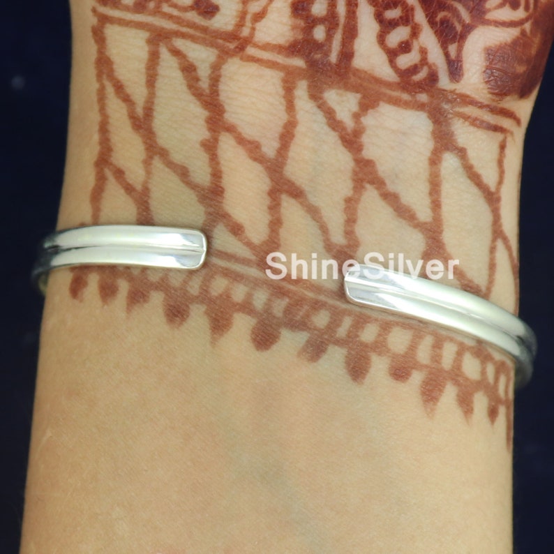 K&ouml;nnte beinhalten: Ein silbernes Armreif-Armband mit glatter, polierter Oberfl&auml;che. Das Armband ist offen und hat ein schlichtes, minimalistisches Design.