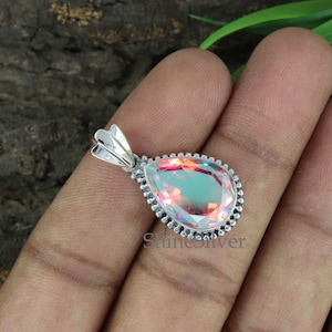 K&ouml;nnte beinhalten: Ein tropfenf&ouml;rmiger Anh&auml;nger mit einem regenbogenfarbenen Edelstein, der in Sterlingsilber gefasst ist. Der Anh&auml;nger hat einen perlenbesetzten Rand und eine silberne &Ouml;se.