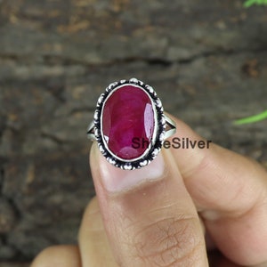May include: A silver ring with a large oval-shaped ruby gemstone. The ring has a beaded edge and a simple band.