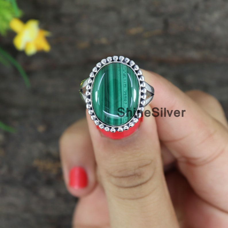 Peut inclure: Une bague en argent avec une pierre ovale en malachite verte sertie dans une b&eacute;li&egrave;re &agrave; perles. La bague est port&eacute;e sur un doigt.