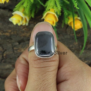 May include: A silver ring with a black rectangular gemstone. The ring is set in a simple band and the gemstone has a smooth, polished surface.