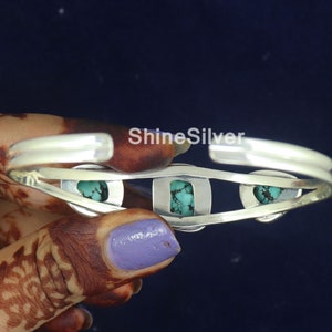 K&ouml;nnte beinhalten: Silberarmband mit drei T&uuml;rkis-Steinen, die in das Metall gefasst sind. Das Armband ist offen und hat ein schlichtes Design.