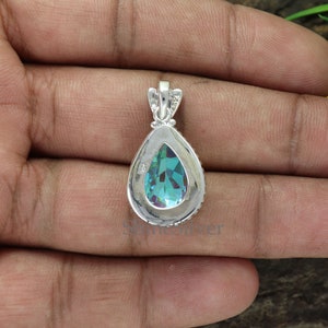 K&ouml;nnte beinhalten: Ein silberner Anh&auml;nger mit einem tropfenf&ouml;rmigen blauen Edelstein. Der Edelstein ist facettiert und in einer silbernen Fassung gefasst. Der Anh&auml;nger hat eine &Ouml;se zum Anbringen an einer Kette.