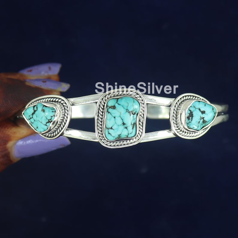 K&ouml;nnte beinhalten: Silberner Armreif mit drei T&uuml;rkis-Steinen. Die Steine sind in Silber gefasst und haben eine strukturierte Oberfl&auml;che. Der Armreif ist offen und verstellbar.