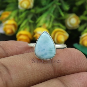 Puede incluir: Un anillo de plata con una piedra preciosa azul y blanca en forma de lágrima. El anillo está en un dedo.