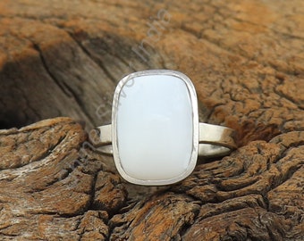 Può includere: Un anello d'argento con una pietra ovale bianca. L'anello è su una superficie di legno.