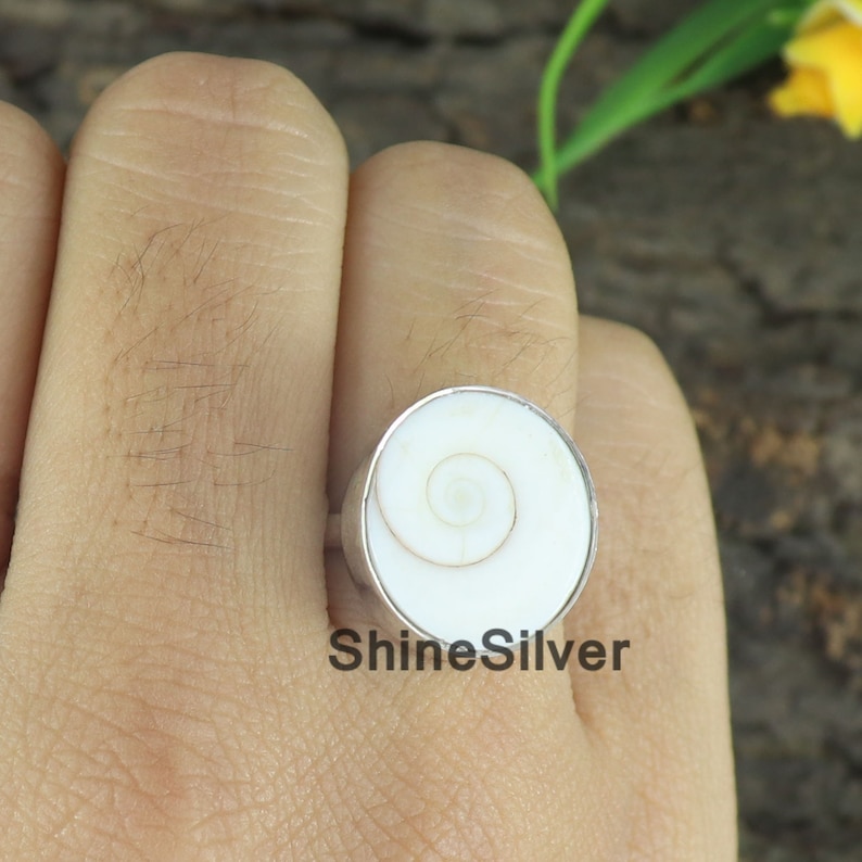 May include: A white shell ring with a silver band. The shell has a spiral pattern in the center.
