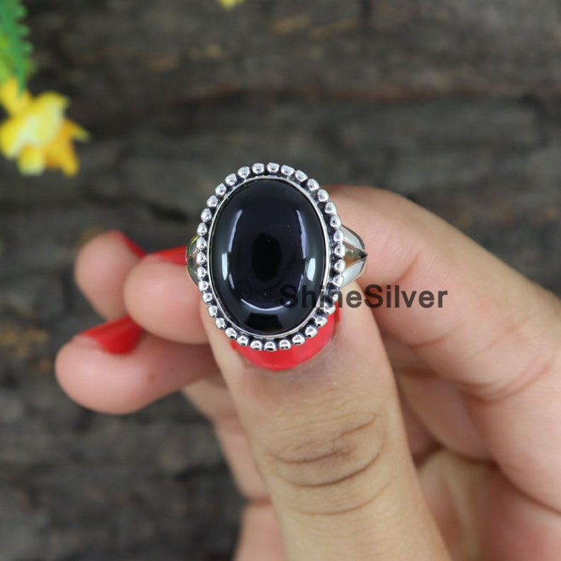 Peut inclure: Une bague en argent avec une pierre ovale noire sertie dans une b&eacute;li&egrave;re &agrave; perles. La bague est sur un doigt.