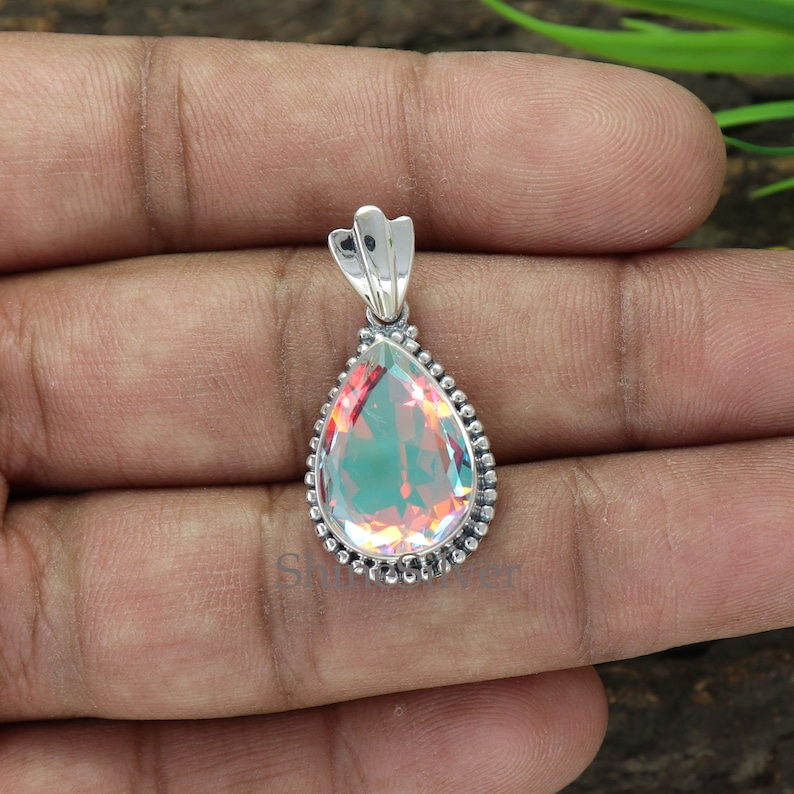 K&ouml;nnte beinhalten: Ein perlmuttartiger tropfenf&ouml;rmiger Edelstein-Anh&auml;nger mit einer silbernen Fassung. Der Anh&auml;nger hat einen perlenbesetzten Rand und eine silberne &Ouml;se.