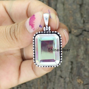 May include: A rectangular pendant featuring an iridescent gemstone set in a silver-toned frame with a beaded edge. The pendant has a small loop for a chain. The text "ShineSilver" is visible on the gemstone, adding a unique detail to the design.