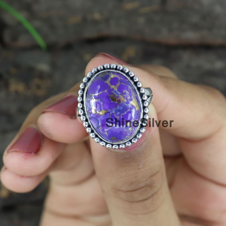 Peut inclure: Une bague en argent avec une pierre ovale de couleur violette et dor&eacute;e sertie dans une b&eacute;li&egrave;re &agrave; perles. La bague est port&eacute;e sur un doigt.