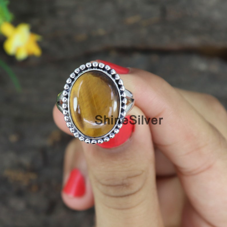 Peut inclure: Une bague en argent avec une pierre pr&eacute;cieuse en &oelig;il de tigre marron sertie dans une b&eacute;li&egrave;re ovale perl&eacute;e. La bague est port&eacute;e sur un doigt.