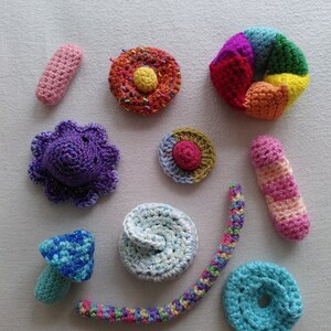May include: A collection of colourful crocheted items, including a mushroom, a doughnut, a flower, a long worm, and a few other shapes.