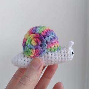 May include: A crocheted snail with a rainbow coloured shell and a white body.