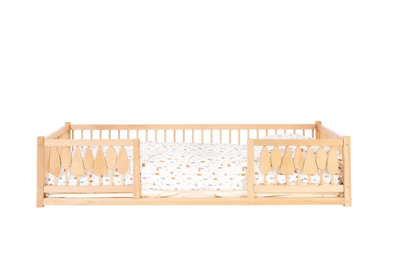Puede incluir: Una cama de madera para ni&ntilde;os peque&ntilde;os con una s&aacute;bana estampada en blanco y marr&oacute;n. La cama tiene una barandilla de seguridad en ambos lados con recortes en forma de hoja.