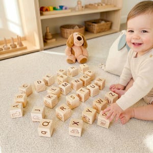 May include: A collection of wooden alphabet blocks, each with a letter and a small animal illustration, are arranged on a cream rug. A soft toy dog and a baby are in the background. The blocks are part of a children's toy.