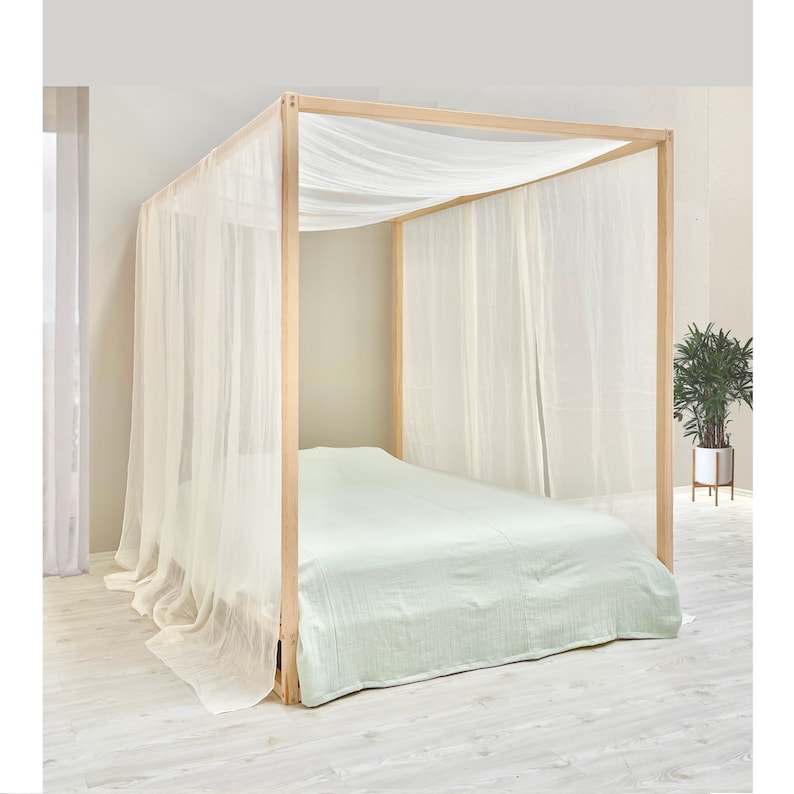 May include: A wooden canopy bed frame with a white sheer canopy and a light green bedspread.