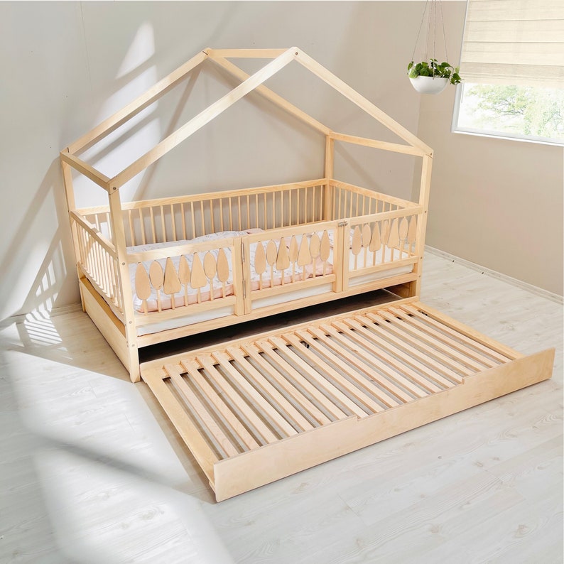 May include: A wooden bed frame with a canopy and a pull-out trundle bed. The bed frame is made of natural wood and has a slatted design. The canopy is made of wood and has a simple, modern design. The trundle bed is also made of wood and has a slatted design.