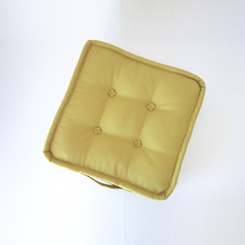 May include: A yellow square floor cushion with a tufted design and a handle. The cushion is made of a soft, textured fabric.