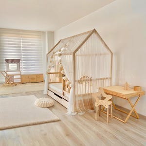 May include: A wooden house-shaped bed frame with a white canopy and a white mattress. The bed is in a light-colored room with a white rug and a wooden desk and chair.